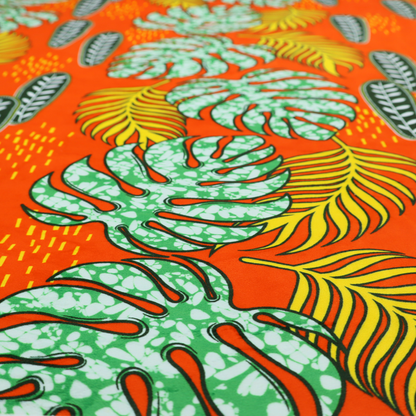Fabric featuring a vibrant, repeating tropical pattern with textured green monstera leaves, yellow ferns, and dark green patterned seed pods on a bright orange background.
