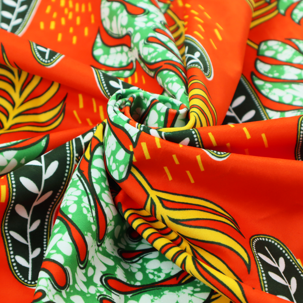 Fabric featuring a vibrant, repeating tropical pattern with textured green monstera leaves, yellow ferns, and dark green patterned seed pods on a bright orange background.
