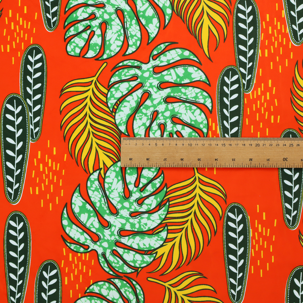 Fabric featuring a vibrant, repeating tropical pattern with textured green monstera leaves, yellow ferns, and dark green patterned seed pods on a bright orange background.