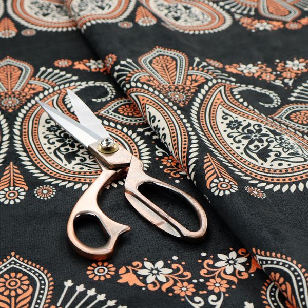 A black fabric pattern featuring elegant horizontal bands of intricate paisley motifs and ornate cross-shaped designs in cream and terracotta orange.