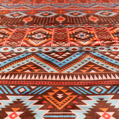 A brown fabric pattern featuring southwest-inspired geometric bands with zigzags, diamonds, and native-style motifs in terracotta, light blue, and cream.