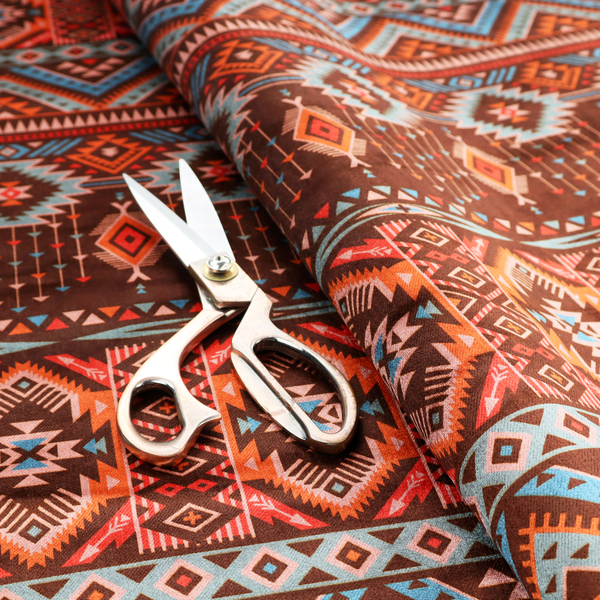 A brown fabric pattern featuring southwest-inspired geometric bands with zigzags, diamonds, and native-style motifs in terracotta, light blue, and cream.