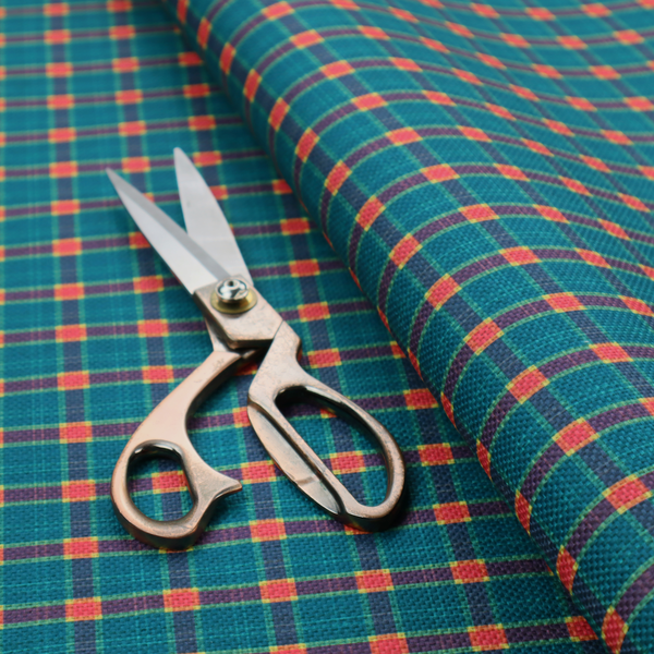 A rich teal plaid fabric pattern featuring a dense grid of intersecting dark blue and thin yellow stripes with bright red square accents.
