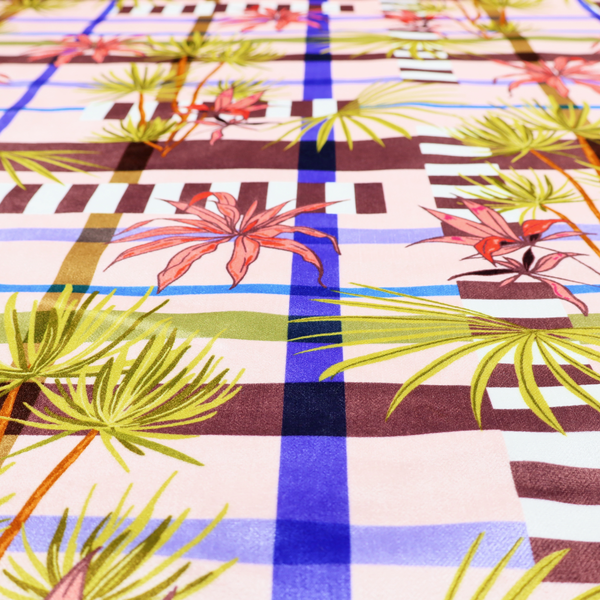 An eclectic, geometric tropical fabric pattern featuring a unique overlay design. The background is a structured windowpane plaid layout composed of intersecting lines in cobalt blue, olive green, and chocolate brown across a dusty pink base. Layered over this grid is a repeating botanical print of tropical plants, featuring fan palms in lime green and slender fronds in terracotta pink.