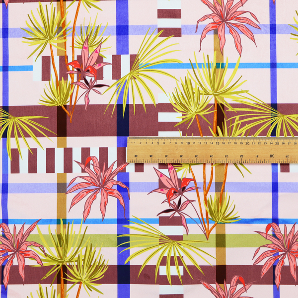 An eclectic, geometric tropical fabric pattern featuring a unique overlay design. The background is a structured windowpane plaid layout composed of intersecting lines in cobalt blue, olive green, and chocolate brown across a dusty pink base. Layered over this grid is a repeating botanical print of tropical plants, featuring fan palms in lime green and slender fronds in terracotta pink.
