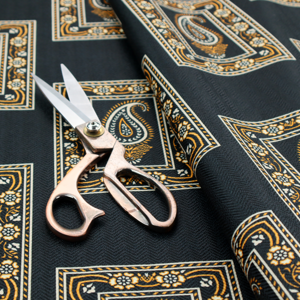 Fabric featuring a traditional repeating pattern of detailed white and gold paisley motifs, each enclosed within an ornate rectangular border on a charcoal black background.