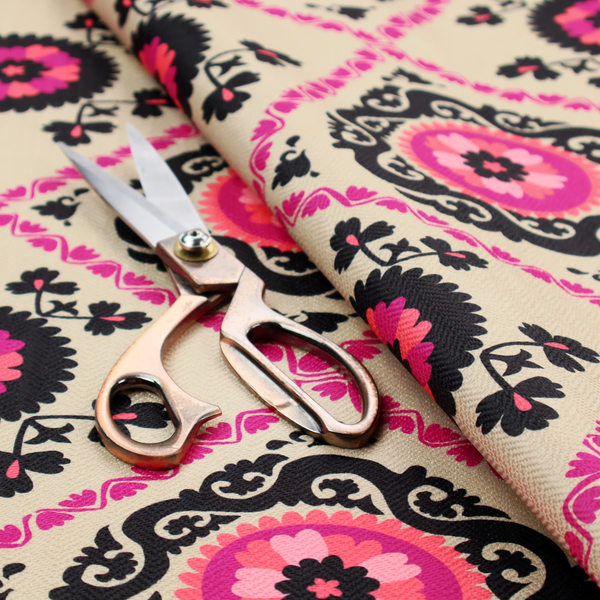 Fabric featuring a vibrant bohemian Suzani-style pattern with bold hot pink and black floral medallions arranged in a diamond lattice on a cream background.