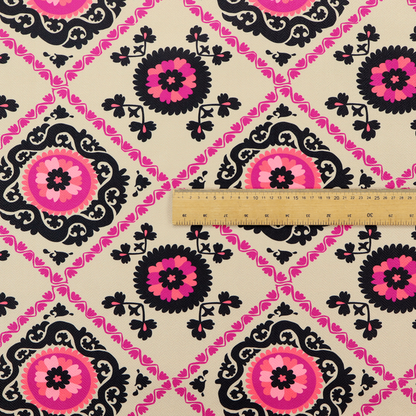Fabric featuring a vibrant bohemian Suzani-style pattern with bold hot pink and black floral medallions arranged in a diamond lattice on a cream background.