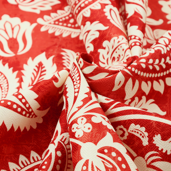 Fabric featuring an ornate repeating pattern of elegant ivory paisley motifs and botanical flourishes over a textured, mottled crimson red background.