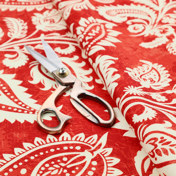 Fabric featuring an ornate repeating pattern of elegant ivory paisley motifs and botanical flourishes over a textured, mottled crimson red background.