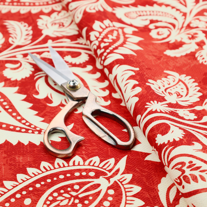Fabric featuring an ornate repeating pattern of elegant ivory paisley motifs and botanical flourishes over a textured, mottled crimson red background.