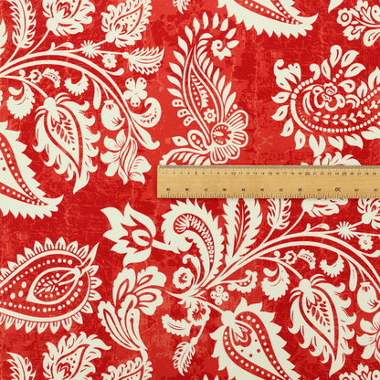 Fabric featuring an ornate repeating pattern of elegant ivory paisley motifs and botanical flourishes over a textured, mottled crimson red background.