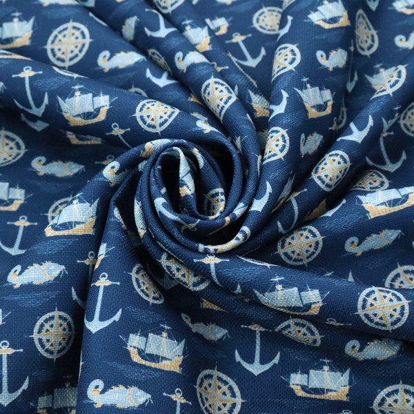 A nautical-themed fabric pattern featuring alternating rows of light blue and gold sailing ships, compass roses, anchors, and fish against a dark blue background.