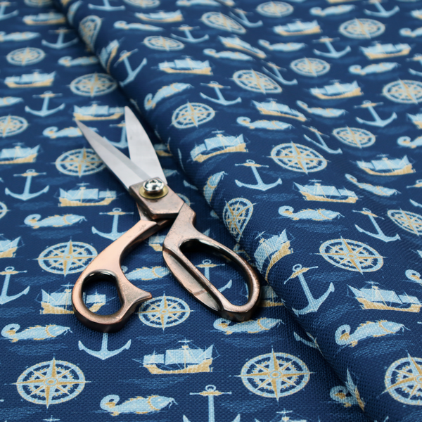 A nautical-themed fabric pattern featuring alternating rows of light blue and gold sailing ships, compass roses, anchors, and fish against a dark blue background.