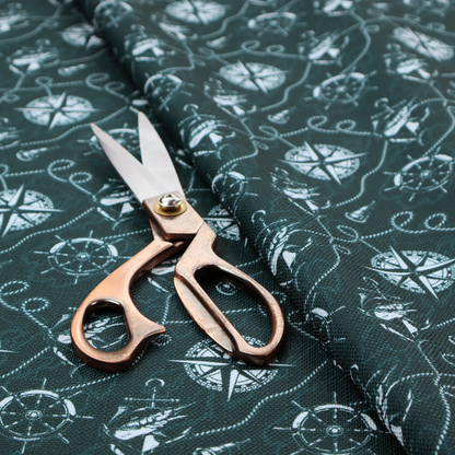 A nautical-themed fabric pattern featuring light blue compass roses, ships, anchors, and intertwined ropes against a dark teal or green background.