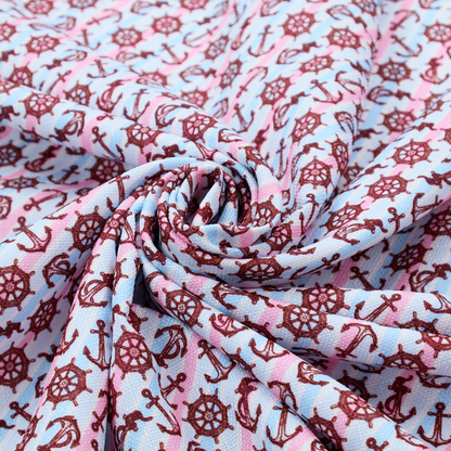 A nautical-themed fabric pattern featuring diagonal stripes in light blue and pink, scattered with dark red ship's wheels and anchors.