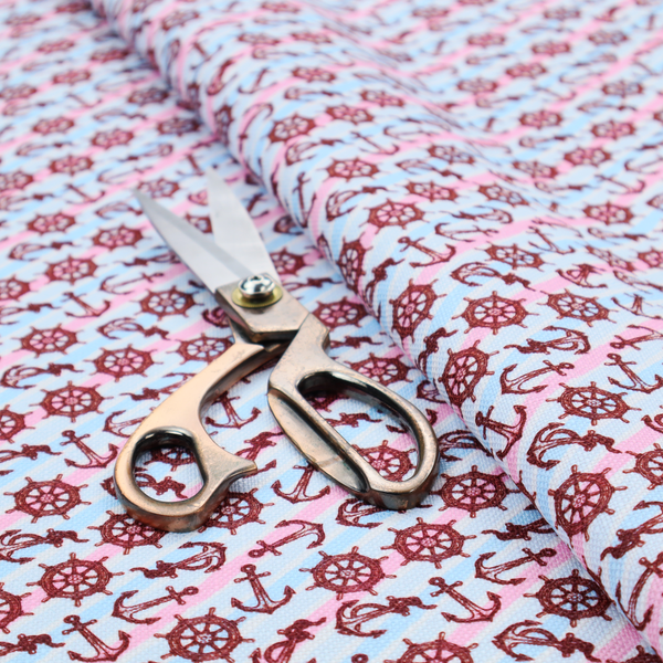 A nautical-themed fabric pattern featuring diagonal stripes in light blue and pink, scattered with dark red ship's wheels and anchors.