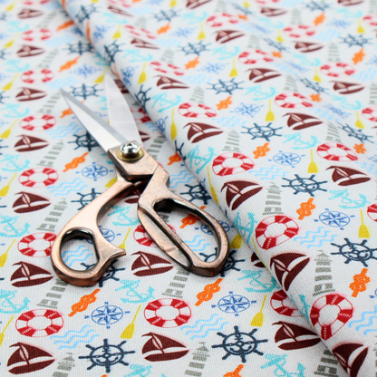 A colourful nautical-themed fabric pattern featuring a repeating mix of lighthouses, sailboats, life rings, ship's wheels, anchors, and waves against a white background.