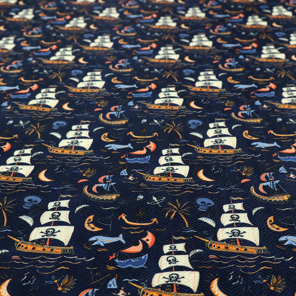 A dark navy blue fabric patterned with a repeating pirate-themed design featuring multi-sailed galleon ships with skull-and-crossbones flags sailing on stylized waves, accompanied by smaller elements including blue whales, crescent moons, skulls, tropical palm trees, and anchors.