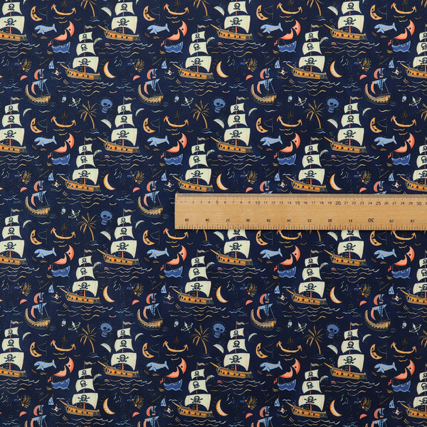 A dark navy blue fabric patterned with a repeating pirate-themed design featuring multi-sailed galleon ships with skull-and-crossbones flags sailing on stylized waves, accompanied by smaller elements including blue whales, crescent moons, skulls, tropical palm trees, and anchors.