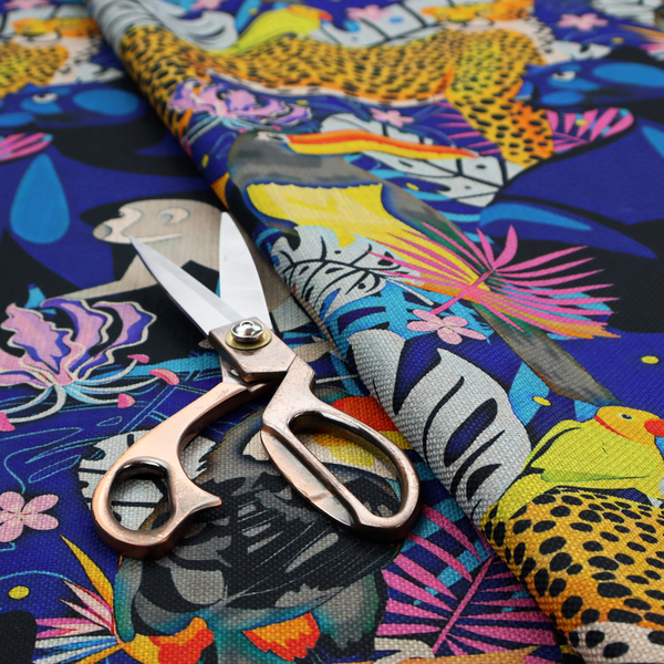 A vibrant jungle-themed fabric on a rich blue background featuring a repeating pattern of yellow leopards with black spots, blue panthers, toucans with bright orange and yellow beaks, light grey monkeys, small yellow-and-red birds, and lush tropical leaves and pink flowers.