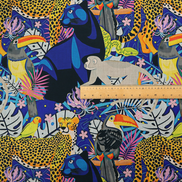 A vibrant jungle-themed fabric on a rich blue background featuring a repeating pattern of yellow leopards with black spots, blue panthers, toucans with bright orange and yellow beaks, light grey monkeys, small yellow-and-red birds, and lush tropical leaves and pink flowers.