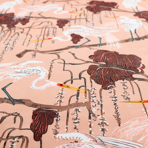A peach-pink fabric with an illustrated botanical and avian pattern featuring white egrets perched on brown branches among dark red, stylized foliage and weeping floral tendrils.