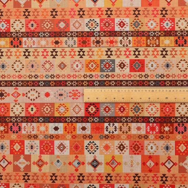 A geometric woven fabric featuring horizontal rows of Aztec and tribal-inspired patterns in warm earthy tones of orange, red, yellow, beige, brown, and dark charcoal.
