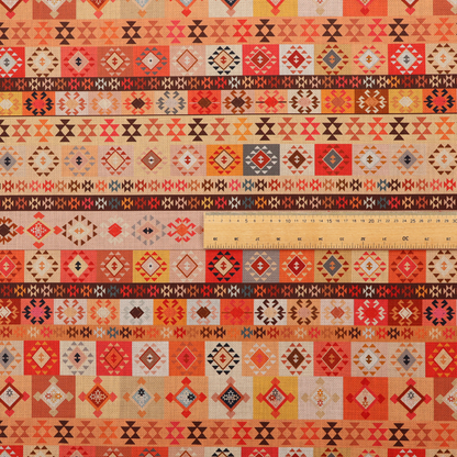 A geometric woven fabric featuring horizontal rows of Aztec and tribal-inspired patterns in warm earthy tones of orange, red, yellow, beige, brown, and dark charcoal.
