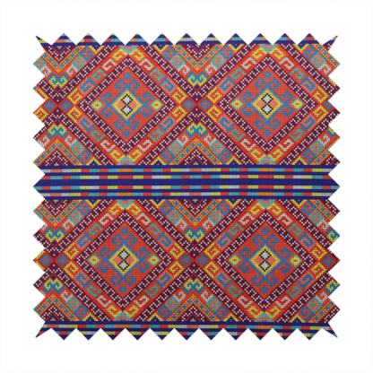 A vibrant geometric fabric featuring a detailed pixelated pattern of large interlocking diamonds in red, blue, purple, yellow, and turquoise, separated by horizontal striped bands of multi-coloured dots on a dark blue background, reminiscent of traditional beadwork or woven textile art.