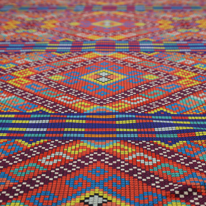 A vibrant geometric fabric featuring a detailed pixelated pattern of large interlocking diamonds in red, blue, purple, yellow, and turquoise, separated by horizontal striped bands of multi-coloured dots on a dark blue background, reminiscent of traditional beadwork or woven textile art.