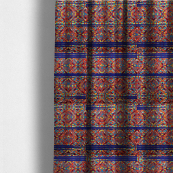 The fabric used to create these made-to-measure curtains is a vibrant geometric fabric featuring a detailed pixelated pattern of large interlocking diamonds in red, blue, purple, yellow, and turquoise, separated by horizontal striped bands of multi-coloured dots on a dark blue background, reminiscent of traditional beadwork or woven textile art.