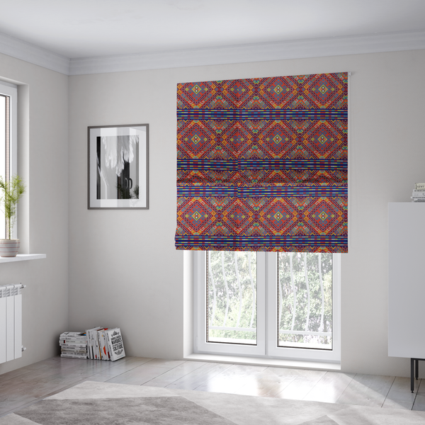 The fabric used to create these Roman blinds is a vibrant geometric fabric featuring a detailed pixelated pattern of large interlocking diamonds in red, blue, purple, yellow, and turquoise, separated by horizontal striped bands of multi-coloured dots on a dark blue background, reminiscent of traditional beadwork or woven textile art.