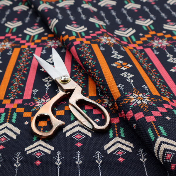 A dark navy blue fabric featuring a repeating geometric pattern with rows of chevron arrows, starburst motifs, and vertical striped panels containing delicate floral vine designs in pink, orange, white, and turquoise.