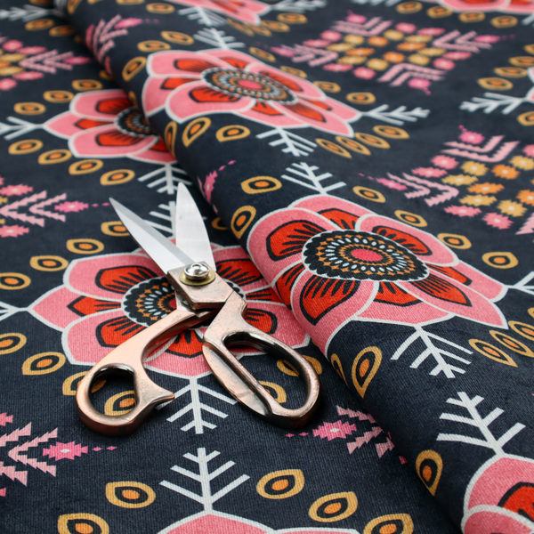 A repeating folk-art textile design featuring alternating rows of stylized pink floral blossoms and intricate diamond-shaped geometric motifs.