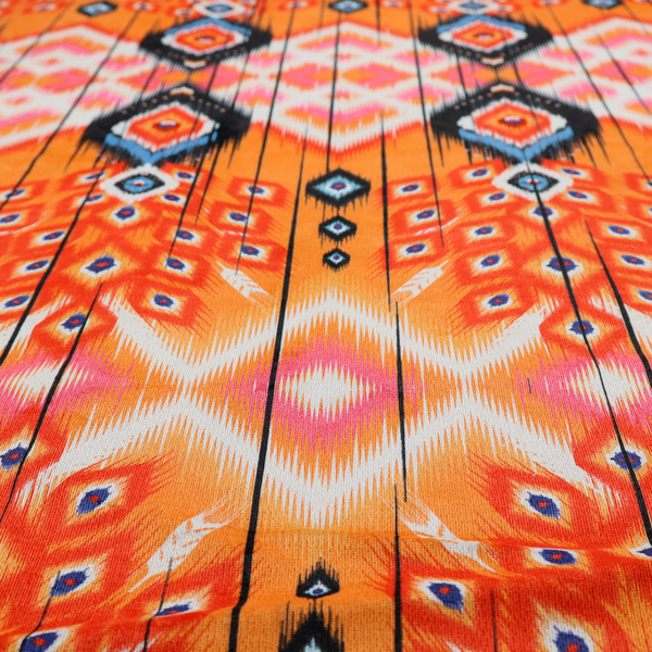 A vibrant orange fabric featuring a bold Southwestern Aztec and ikat-style geometric pattern.