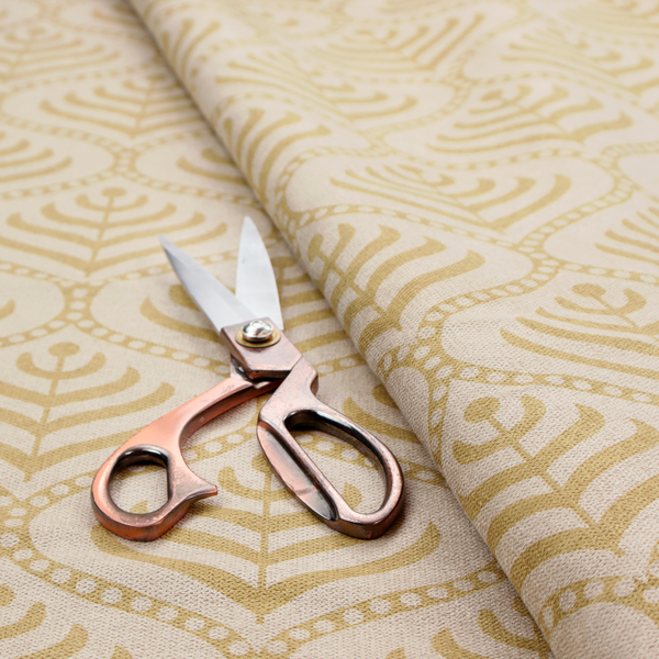 A decorative, vintage-inspired textile pattern characterized by repeating ogival ogee arches filled with stylized leaf or feather motifs and dotted framing lines, rendered in gold or mustard yellow on a light neutral background.
