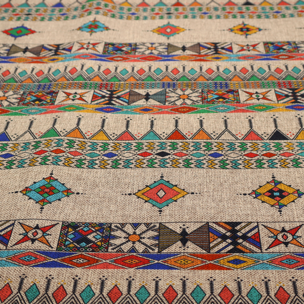 A multi-coloured ethnic geometric fabric with repeating rows of colourful tribal diamonds, zigzags, and striped borders set against a light neutral background.