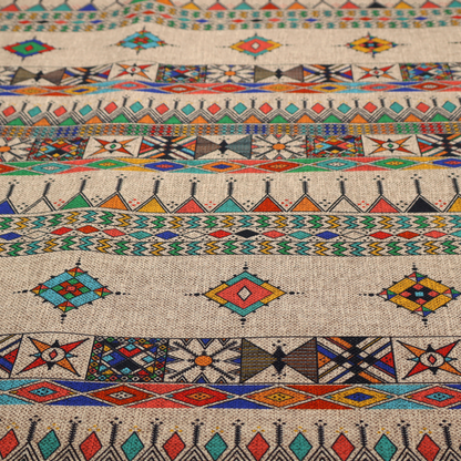 A multi-coloured ethnic geometric fabric with repeating rows of colourful tribal diamonds, zigzags, and striped borders set against a light neutral background.