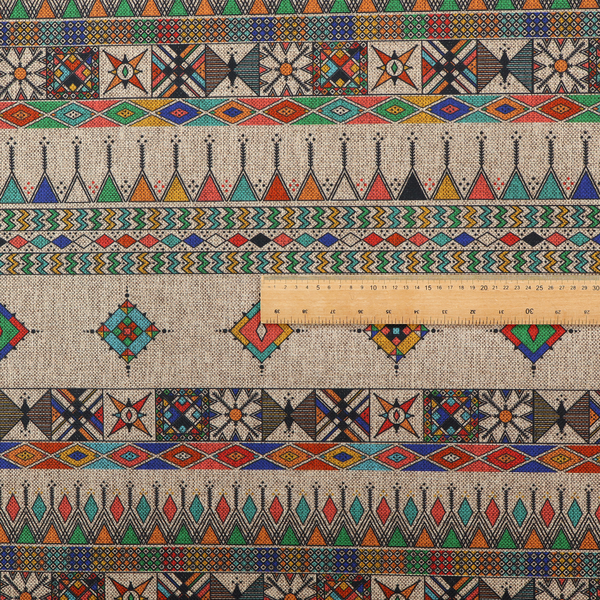 A multi-coloured ethnic geometric fabric with repeating rows of colourful tribal diamonds, zigzags, and striped borders set against a light neutral background.