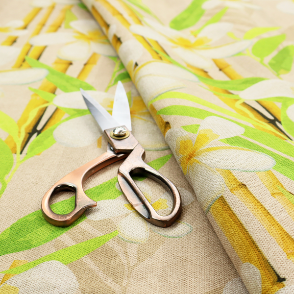 A tropical botanical fabric pattern with white plumeria blossoms featuring yellow centres, paired with green leaves and yellow bamboo stalks, set against a light beige background.