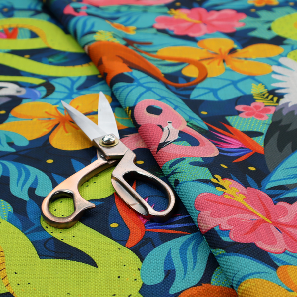 Vibrant jungle fabric pattern featuring neon green snakes, orange monkeys, pink flamingos, and harpy eagles surrounded by tropical flowers and blue foliage on a dark blue background.
