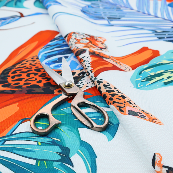 Pattern fabric featuring leopards resting on orange branches amidst vibrant blue and turquoise tropical leaves and foliage against a light background.