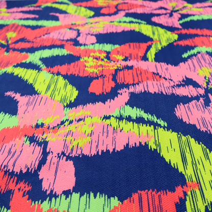 A vibrant fabric pattern featuring large coral and light pink lily flowers with bright lime green leaves against a solid royal blue background.