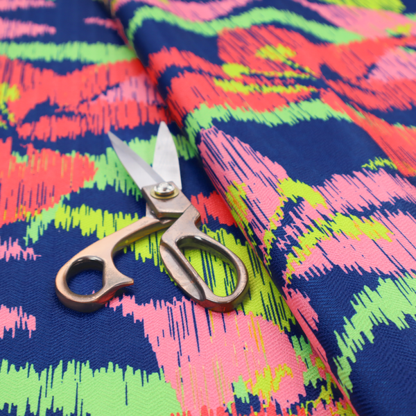 A vibrant fabric pattern featuring large coral and light pink lily flowers with bright lime green leaves against a solid royal blue background.