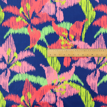 A vibrant fabric pattern featuring large coral and light pink lily flowers with bright lime green leaves against a solid royal blue background.