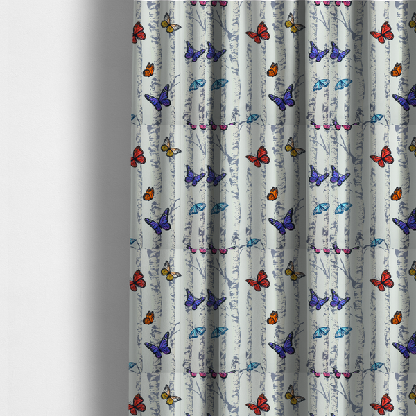 The fabric used to create these made-to-measure curtains is a light-coloured fabric featuring a pattern of vertical grey and white birch tree trunks interspersed with colourful butterflies in shades of red, orange, yellow, blue, and purple.