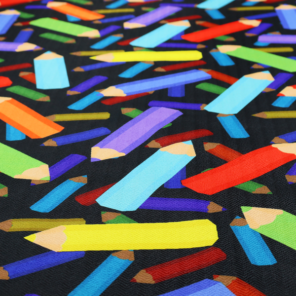 A black fabric featuring a playful, repeating pattern of coloured pencils in various shades including red, yellow, light blue, green, purple, and orange scattered diagonally across the background.