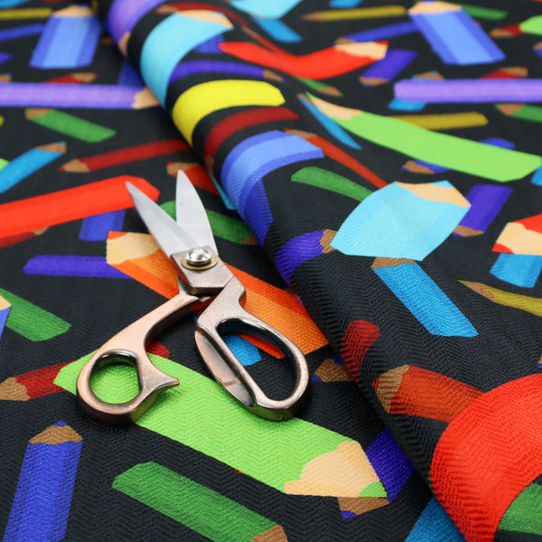 A black fabric featuring a playful, repeating pattern of coloured pencils in various shades including red, yellow, light blue, green, purple, and orange scattered diagonally across the background.