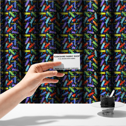 The fabric used to create these made-to-measure curtains is a black fabric featuring a playful, repeating pattern of coloured pencils in various shades including red, yellow, light blue, green, purple, and orange scattered diagonally across the background.
